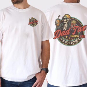 Pu&ograve; includere: T-shirt bianca con grafica sul davanti e sul retro. La grafica anteriore &egrave; uno scheletro con la scritta "Dad Tax". La grafica posteriore presenta uno scheletro con una bevanda e patatine fritte, e la scritta "Dad Tax, Making Sure It's Not Poison".