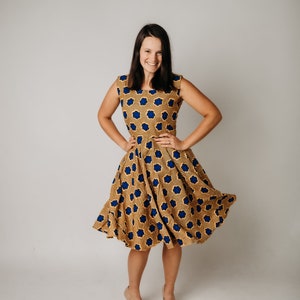 May include: A sleeveless dress with a brown and blue floral pattern. The dress has a fitted bodice and a flared skirt. The model is wearing nude-colored heels. The dress is knee-length and appears to be made of cotton or a similar fabric.