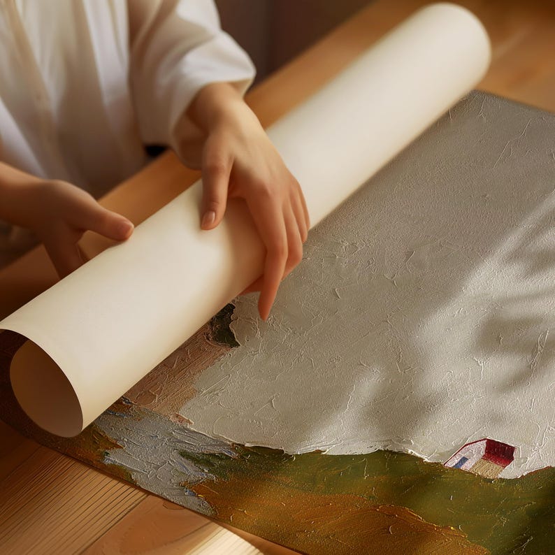 May include: A person is rolling up a white canvas painting with a landscape scene. The painting features a green field, a small white house with a red roof, and a blue sky with white clouds.