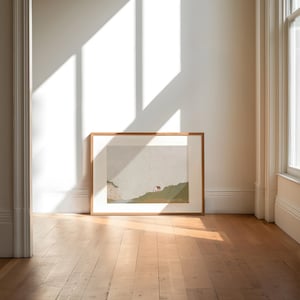 May include: A framed landscape painting of a green hillside with a small white house and a cliff in the distance. The painting is in a light wood frame and is hanging on a white wall.