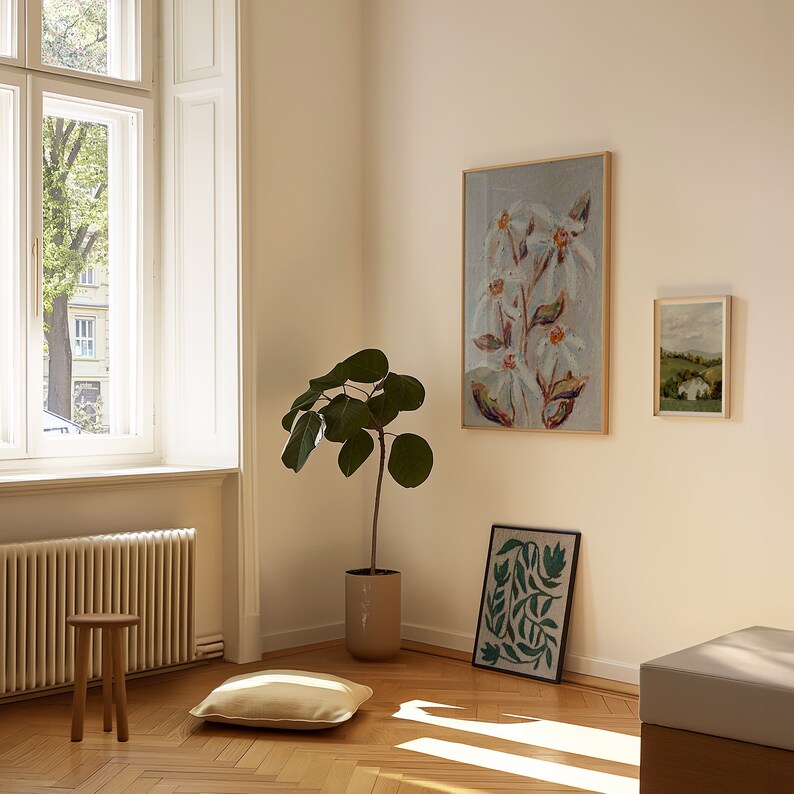 May include: A white room with a large window, a potted plant, a wooden stool, a beige cushion, and three framed art prints. The art prints feature a floral design, a landscape scene, and a green and blue abstract design.