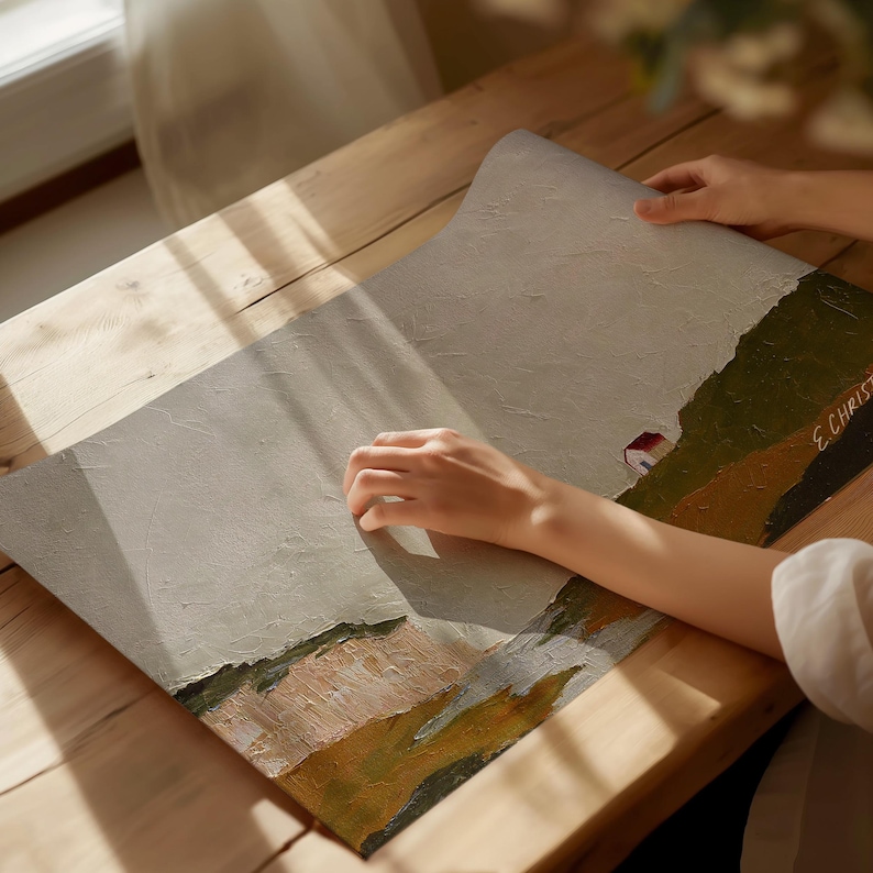 May include: A hand holds a painting of a landscape with a small house and a field. The painting is on a wooden surface. The artist's signature, "E. Christ", is visible in the bottom right corner.