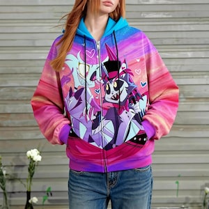 Op de afbeelding: Een hoodie met ritssluiting met een levendig cartoonontwerp in paars, roze en blauw. De hoodie heeft een blauwe capuchon en manchetten en een ritssluiting over de hele lengte. Het ontwerp bevat harten en een kleurrijke zonsondergangachtige achtergrond.