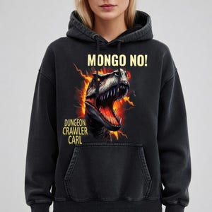 May include: Black hooded sweatshirt with a dinosaur graphic and the text "MONGO NO!" and "DUNGEON CRAWLER CARL" in yellow. The dinosaur graphic has red and orange flames in the background.