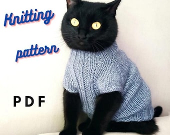 May include: A black cat wearing a light blue knitted sweater. The sweater has a cable knit pattern. The image includes the text "Knitting pattern PDF".