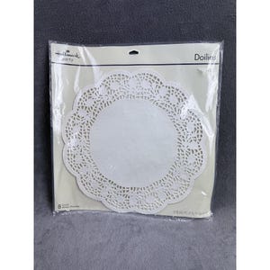 May include: A package of white paper doilies with a scalloped edge and a floral lace design. The package is labeled "Hallmark party" and contains 8 doilies. The doilies are in a clear plastic package.