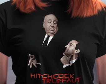 Może przedstawiać: Czarny t-shirt z krótkim rękawem z nadrukiem graficznym przedstawiającym Alfreda Hitchcocka i François Truffauta. Projekt zawiera napis HITCHCOCK TRUFFAUT czerwonymi literami pod portretami dwóch mężczyzn w czarnych garniturach i krawatach.