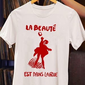 Customized white T-shirt from La Beauté est dans la rue hanging on a hanger