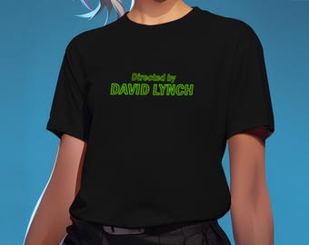 May include: A black short-sleeved t-shirt featuring the text Directed by DAVID LYNCH printed in a bright green font across the chest. The shirt has a crew neckline and a standard fit, showcasing the bold green lettering against the solid black fabric.