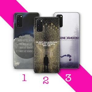 Op de afbeelding: Drie verschillende telefoonhoesjes met verschillende ontwerpen. De eerste hoes heeft een grijze achtergrond met witte tekst die "When you feel my heart, look into my eyes, it's where my demons, it's where my demons" luidt. De tweede hoes heeft een gouden achtergrond met zwarte tekst die "Oh don't you understand, I'm never changing who I am" luidt. De derde hoes heeft een grijze achtergrond met de naam van een band en de titel van een album in witte tekst die "Imagine Dragons, Continued Silence EP" luidt.