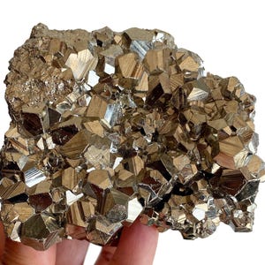 May include: A cluster of pyrite crystals, also known as fool's gold, with a metallic gold color and a geometric, cubic structure. The crystals are tightly packed together, creating a textured surface. The mineral specimen is held in a hand.