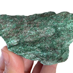 Pode incluir: Uma formação rochosa texturizada, predominantemente verde com manchas prateadas. A forma irregular do mineral é visível, com uma superfície rugosa e estrutura cristalina. A rocha é segurada na mão, destacando sua forma natural. A superfície tem uma qualidade ligeiramente reflexiva.