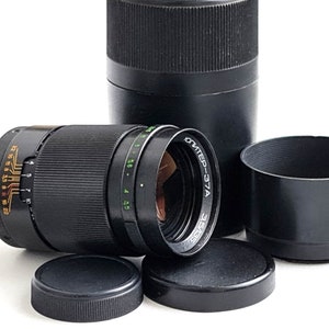 May include: A black camera lens with a silver band and the text "Юпитер-37A 35/65" printed on the side. The lens is surrounded by black lens caps and a black lens hood.