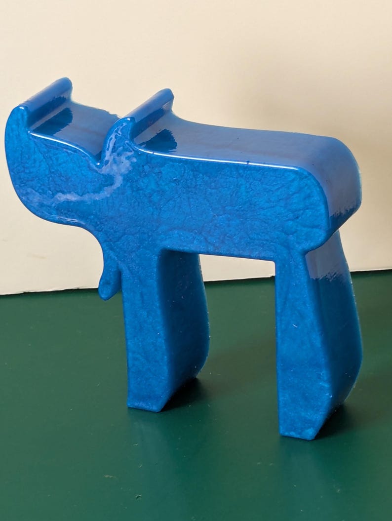 May include: A blue ceramic sculpture of the Hebrew letter 'Chai', which means 'life' in Hebrew. The sculpture is made of a smooth, glossy ceramic and has a slightly textured surface.