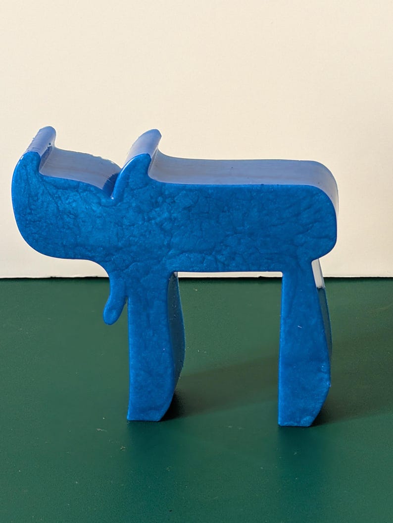 May include: A blue, three-dimensional, plastic sculpture of the Hebrew letter 'Chai' which means 'life' in Hebrew.