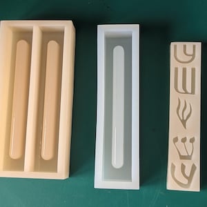 May include: Three silicone molds in a row. The first mold is rectangular with two rounded, cylindrical cavities. The second mold is a long, rectangular shape with a single, rounded cavity. The third mold is a rectangular shape with Hebrew letters and symbols.