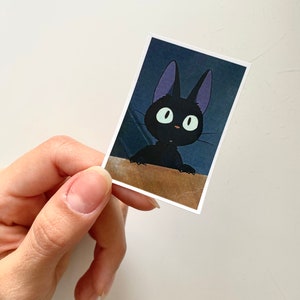 May include: A black cat with large, round eyes and purple ears. The cat is looking up and to the right. The image is a close-up of the cat's face.