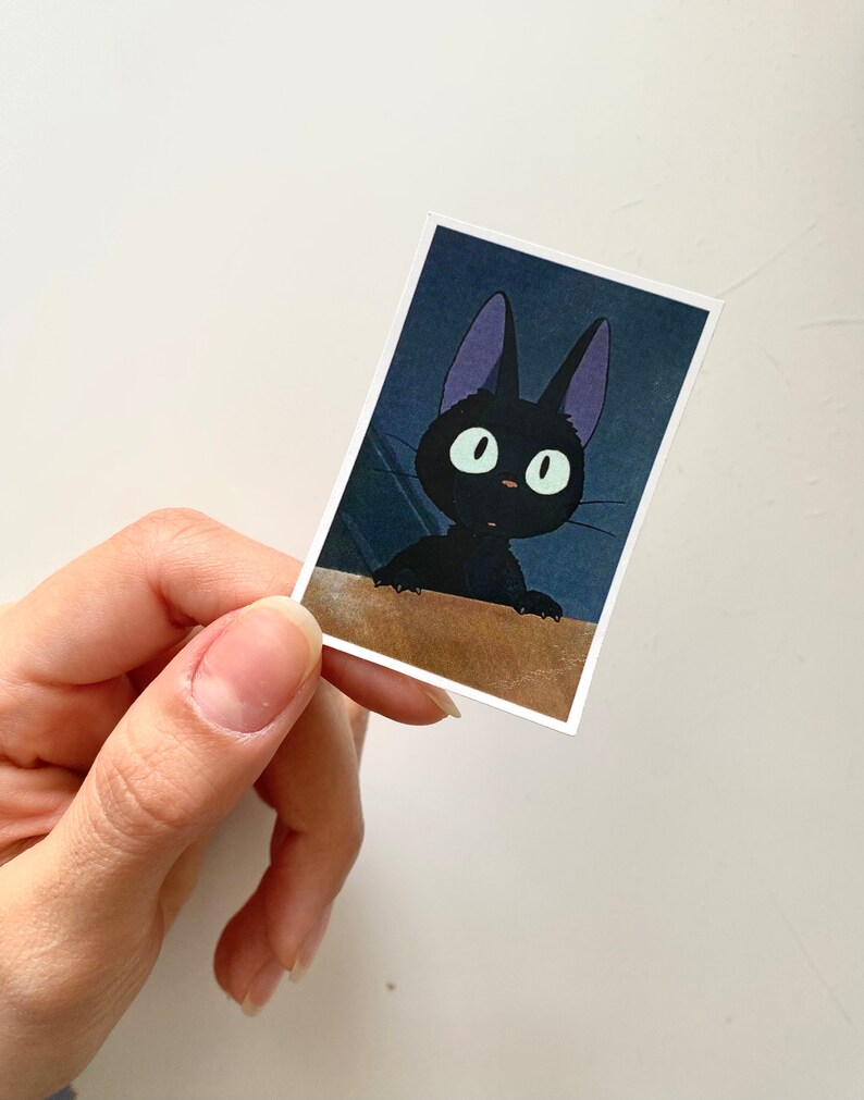 May include: A black cat with large, round eyes and purple ears. The cat is looking up and to the right. The image is a close-up of the cat's face.