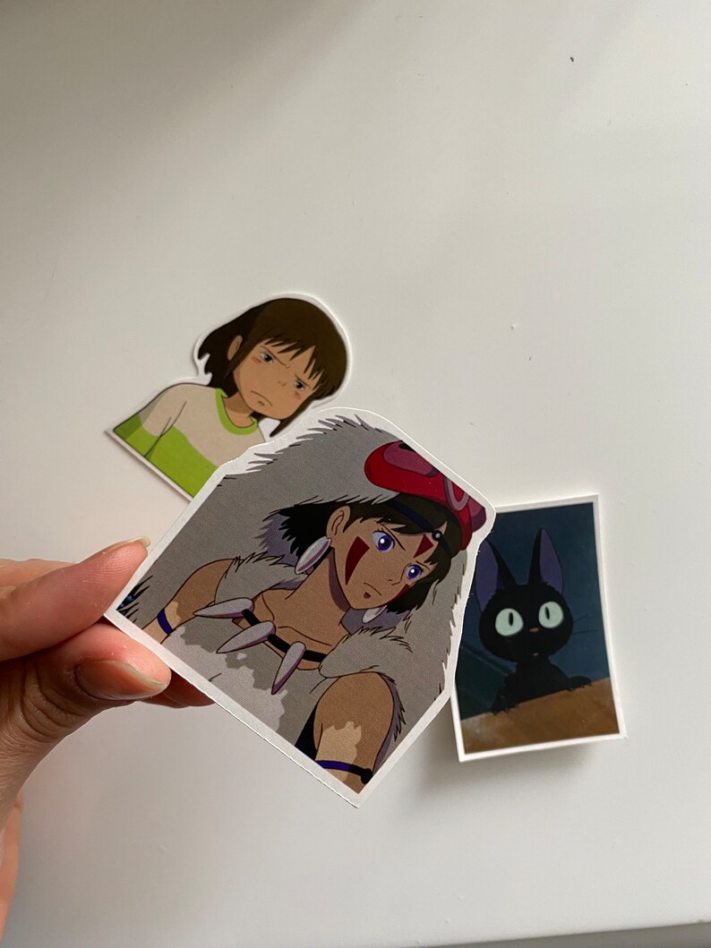 May include: Three anime stickers featuring characters from the movie Princess Mononoke. The first sticker shows a young girl with brown hair and a green shirt. The second sticker shows a young woman with brown hair and a white fur coat. The third sticker shows a black cat with green eyes.