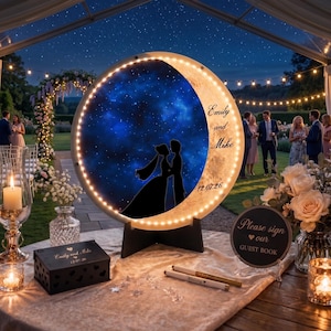 Könnte beinhalten: Ein kreisförmiges, beleuchtetes Schild mit einem blauen Sternenhimmel und der schwarzen Silhouette eines Paares. Das Schild zeigt den Text 'Emily and Mike' und '12.07.26'. Es enthält eine passende schwarze Holzbox und ein rundes Schild mit der Aufschrift 'Please sign our GUEST BOOK'.