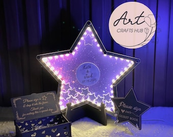 May include: A large, illuminated star-shaped guest book with a purple galaxy design and the names "Kath & Jack" and the date "07.15.2025". Includes a wooden box and a smaller star-shaped sign that says "Please sign our guest book".