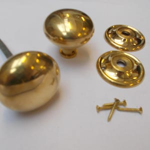 Könnte beinhalten: Eine Sammlung goldfarbener Türbeschläge, darunter zwei runde Türknöpfe, zwei kreisförmige Rosetten und Schrauben. Die Teile sind wahrscheinlich aus Messing oder einem ähnlichen Metall gefertigt. Die Knöpfe haben einen Durchmesser von etwa 5 cm.