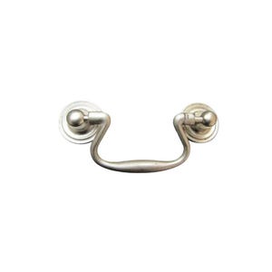 Puede incluir: Un tirador de cajón plateado con un asa curvada y dos placas traseras circulares. El herraje tiene un diseño clásico, adecuado para armarios o muebles. El acabado metálico parece cepillado o mate.