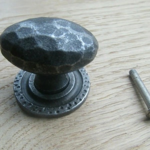 Könnte beinhalten: Ein dunkelgrauer, gehammerter Metallschrankknauf mit passendem Sockel und einer silbernen Schraube. Der Knauf hat eine ovale Form und eine strukturierte Oberfläche. Der Sockel hat einen dekorativen, gepunkteten Rand.