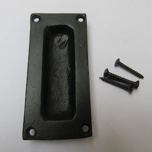 Könnte beinhalten: Schwarzer Einlassgriff aus Gusseisen mit rechteckiger Form und gewölbtem Innenraum. Drei schwarze Schrauben sind im Lieferumfang enthalten. Der Griff hat vier Schraubenlöcher zur Montage. Diese Hardware ist für Schranktüren und Schubladen geeignet.