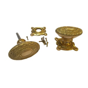 Könnte beinhalten: Verzierte Türknöpfe aus Messing mit ovalem Design und dekorativen Details. Das Set enthält zwei Knöpfe, eine Montageplatte und Schrauben. Die Knöpfe haben eine Vintage-Ästhetik und sind wahrscheinlich für Innentüren.