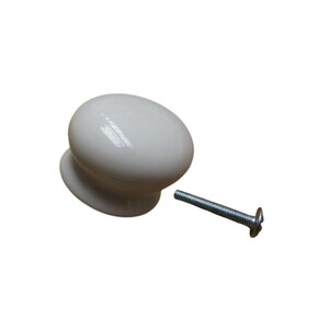 Könnte beinhalten: Ein weißer, ovaler Schrankknauf mit passendem Sockel. Eine silberne Schraube befindet sich rechts vom Knauf. Der Knauf hat eine glänzende Oberfläche und ist wahrscheinlich aus Keramik oder Porzellan.