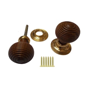 Pode incluir: Conjunto de dois puxadores de porta de madeira com design ranhurado, bases de latão e parafusos correspondentes. Os puxadores são de cor castanho escuro e o latão tem um tom dourado. O conjunto inclui duas rosetas e cinco parafusos.