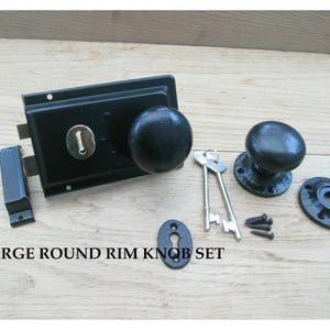 Könnte beinhalten: Ein schwarzes Türknauf-Set mit rundem Knauf-Design. Das Set enthält ein Schloss, zwei Schlüssel, eine Schließplatte und Montagematerial. Der Text "LARGE ROUND RIM KNOB SET" ist sichtbar.