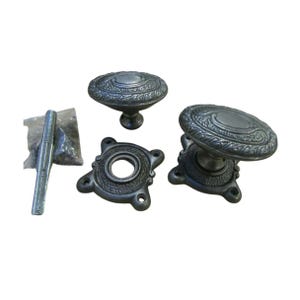 Könnte beinhalten: Antik-Stil Türbeschlagsatz. Das Set enthält zwei ovale Türknöpfe, einen runden Türknauf, eine Montageplatte und ein Schraubenpaket. Die Hardware besteht aus dunklem Metall mit einem verzierten, geprägten Design.
