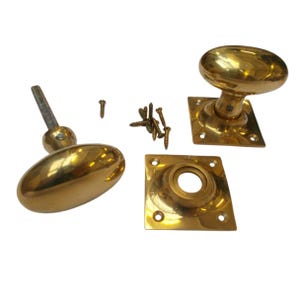 Könnte beinhalten: Ein Satz antiker Türbeschläge aus Messing, darunter zwei ovale Türknöpfe, zwei quadratische Rosetten und mehrere Schrauben. Die Beschläge haben eine polierte, reflektierende Oberfläche.