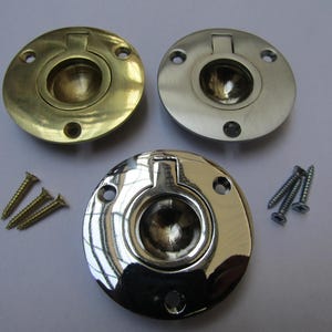 Könnte beinhalten: Drei runde, eingelassene Zugringe in Messing, Nickel und Chrom. Jeder Ring hat einen zentralen, konkaven Zug und eine kreisförmige Basis mit Schraubenlöchern. Schrauben sind enthalten.