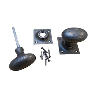 Könnte beinhalten: Antikes Türknauf-Set mit ovalem Knaufdesign. Das Set enthält zwei Knöpfe, zwei quadratische Rückplatten und Schrauben. Die Hardware hat eine verwitterte, metallische Oberfläche, die eine gealterte Ästhetik suggeriert. Ideal für Vintage-Wohnkultur.