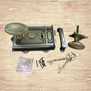 Könnte beinhalten: Ein Türschloss-Set im antiken Stil mit einem ovalen Türknauf, einem rechteckigen Schlosskörper, einer Falle und einem kleineren runden Türknauf. Enthält zwei Schlüssel, Schrauben und ein Schließblech. Das Set ist aus Messing mit gealterter Oberfläche.