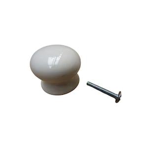 Könnte beinhalten: Ein cremefarbener, oval geformter Schrankknopf mit passendem Sockel. Rechts vom Knopf befindet sich eine silberne Schraube. Der Knopf ist wahrscheinlich aus Keramik oder Porzellan und für Möbel bestimmt.