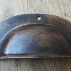 May include: A rustic, antique-style drawer pull with a semi-circular design. The metal hardware has a distressed, bronze finish and three pre-drilled holes for mounting. This cabinet pull is a decorative accent for furniture.
