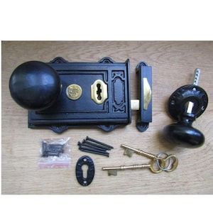 Könnte beinhalten: Ein schwarzes Türschloss-Set aus Gusseisen mit rundem Türknauf, Schließblech und zwei Schlüsseln. Das Set enthält Schrauben und eine Schlüssellochabdeckung. Das Schloss hat ein messingfarbenes Schlüsselloch und Akzente.