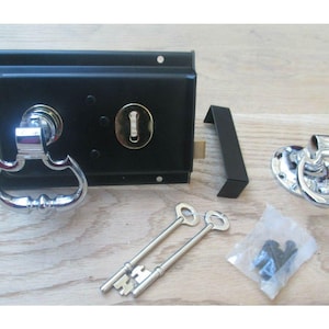 Könnte beinhalten: Ein schwarzes Türschloss-Set mit poliertem Chromgriff und Zierleiste. Enthält zwei Schlüssel, ein Schließblech und Montagematerial. Das Schloss hat ein Schlüsselloch und einen dekorativen Griff.