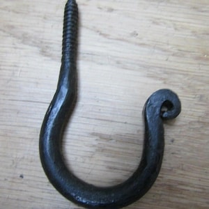 Peut inclure: Un crochet en fer forgé noir, avec un filetage à vis en haut pour une installation facile. Le crochet présente un design incurvé avec une extrémité bouclée décorative, parfait pour suspendre des objets. Le crochet est présenté sur un fond en bois clair.