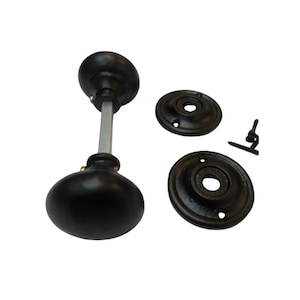 May include: A set of black door hardware, including a doorknob with a silver rod, two circular backplates, and a screw. The doorknob has a rounded shape. The hardware is likely for a vintage or antique door.