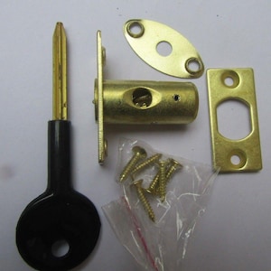 May include: A brass-colored door lock set, including a cylindrical lock body, strike plate, and key. The set also includes an oval-shaped plate and a small bag of screws. The key has a black handle.