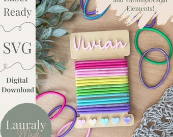 May include: A wooden hair tie holder with the name "Vivian" printed on it. The holder has a rainbow assortment of hair ties and five small heart-shaped decorations at the bottom.