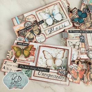 May include: A collection of decorative butterfly-themed tags and embellishments. The tags feature butterfly illustrations, floral backgrounds, and vintage-style text elements. Colors include cream, brown, blue, and orange. The word "Magic" is visible on one tag.
