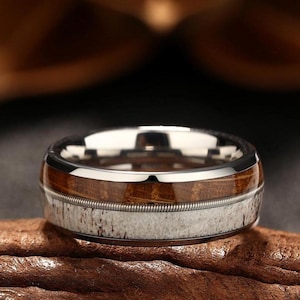 以下が含まれることがあります： 茶色の木と白い鹿の角のインレイが付いた銀のリング。リングは木と鹿の角の周りに薄い銀のバンドがあります。