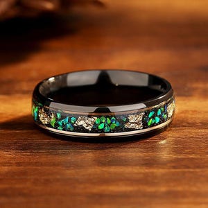 以下が含まれることがあります： 緑と金のインレイが施された黒いリング。リングは耐久性のある素材で作られており、磨かれた仕上げになっています。