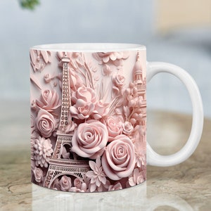 May include: A white ceramic mug with a pink floral design featuring a 3D Eiffel Tower and other floral elements. The mug has a handle on the right side.